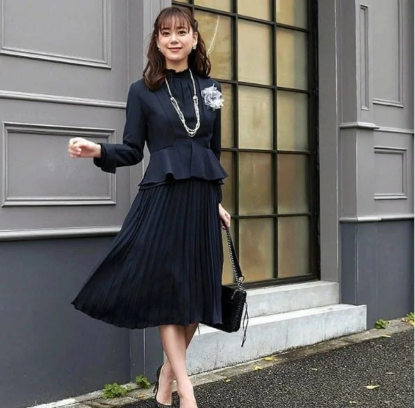 卒業式にネイビーのペプラムジャケットとプリーツスカートを着た女性