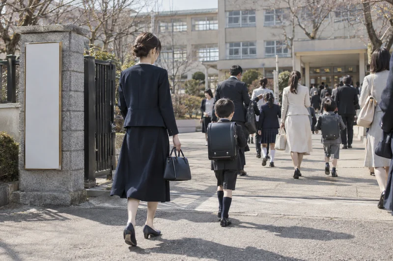 ネイビーのジャケットとワンピースで子どもと校門をくぐる、卒業式・入学式のママ