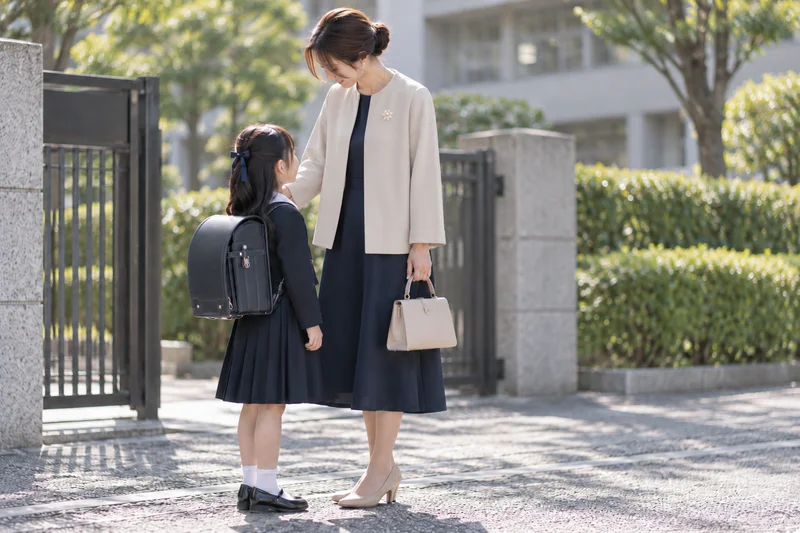ネイビーのワンピースにゆったりしたベージュのジャケットを合わせて入学式に向かう母親と子ども