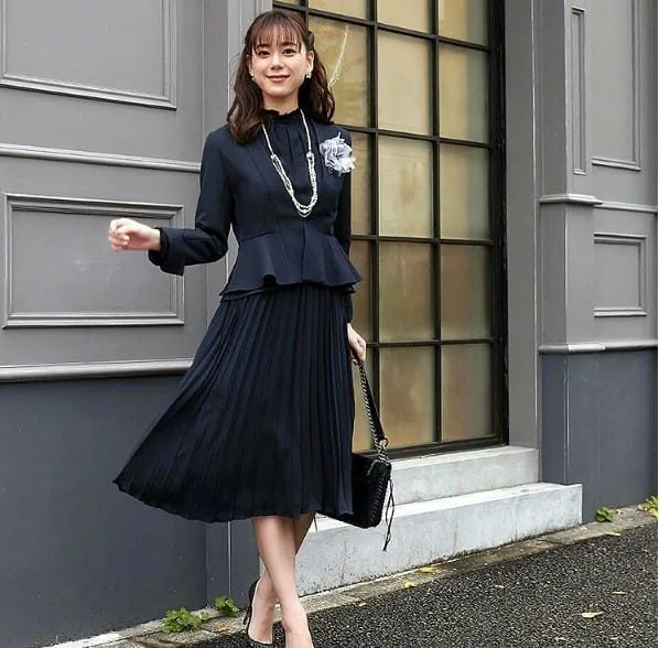 ネイビーのペプラムジャケットとプリーツスカートを合わせた女性のセレモニースーツコーディネート
