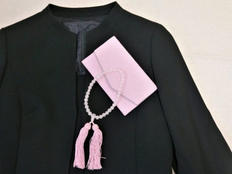 黒の喪服ジャケットにピンクの数珠と袱紗を合わせたお葬式の持ち物イメージ