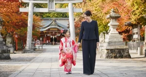 七五三の母親の服装|ネイビーのパンツスーツを着たママと着物姿の子どもが神社を歩く様子