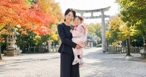 七五三の境内でパンツスーツを着た母親が子どもを抱っこしている様子