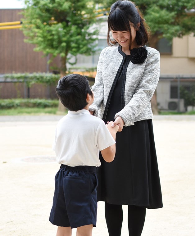 七五三や入学式にぴったりなフォーマルスタイルのママ。グレーのジャケットに黒ワンピースを合わせ、子どもと手をつなぐ微笑ましいシーン。