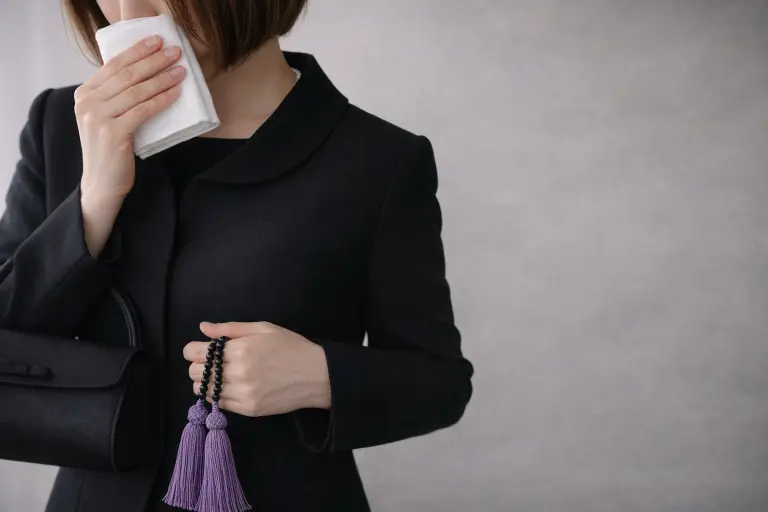 喪服姿でハンカチと数珠を持つ女性