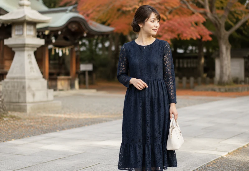 紅葉を背景に佇む紺のレースワンピース姿の女性|秋のお宮参りマナー