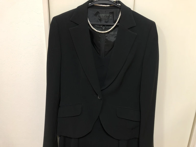 ハンガーにかけた黒いパンツスーツの喪服｜パールネックレスを添えたコーディネート