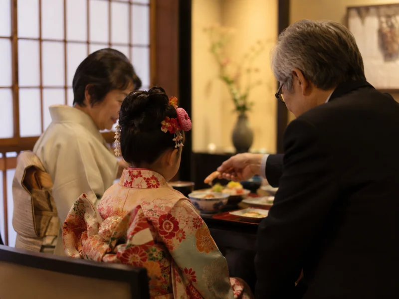食事会で孫の世話をする祖父母と七五三の女の子