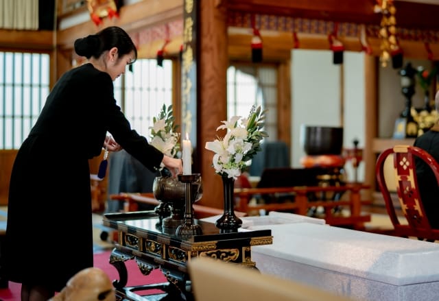 お葬式の祭壇前で手を合わせる黒喪服姿の女性