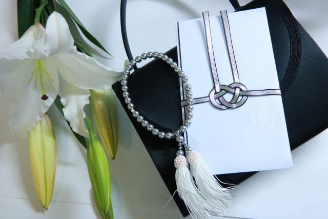 黒のフォーマルバッグの上に香典袋と数珠を置いたお通夜の持ち物セット