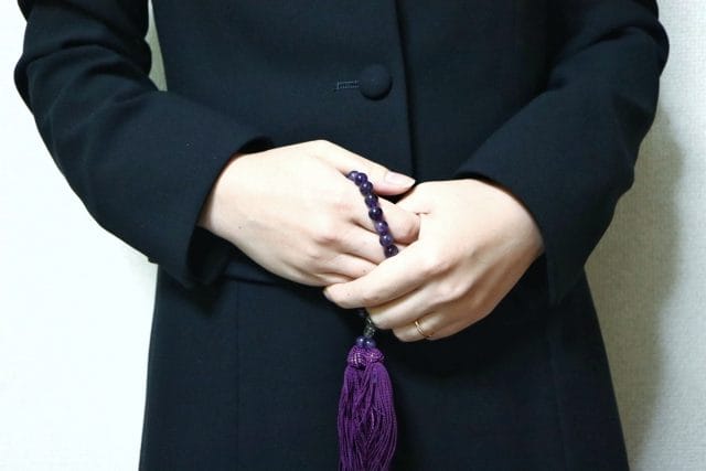 喪服姿の女性が紫の数珠を両手で持つ葬儀参列シーン