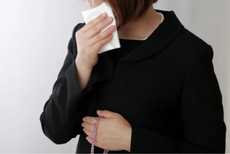 喪服姿の女性が白いハンカチを顔に当てている｜数珠を持ったお葬式参列シーン