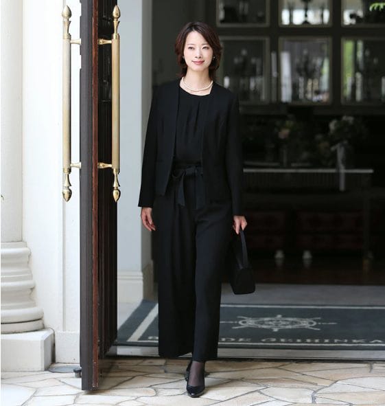 黒のフォーマルパンツスーツを着た女性が屋内に入るシーン。上品で落ち着いた印象