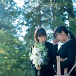 葬儀で花を持つ母と娘　ブラックフォーマルを着た女性たちのイメージ